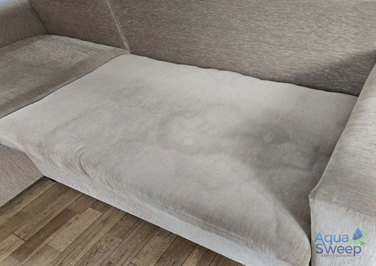 Before: beige fabric corner sofa with a large dark stain across the chaise seat