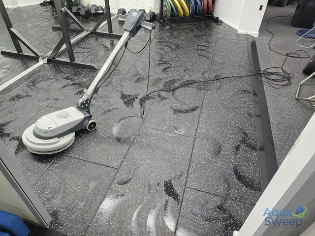 Floor machine scrubbing the rubber floor of a gym at night
