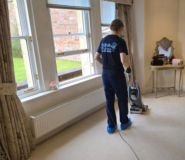 AquaSweep team member vacuuming a cream bedroom carpet before cleaning